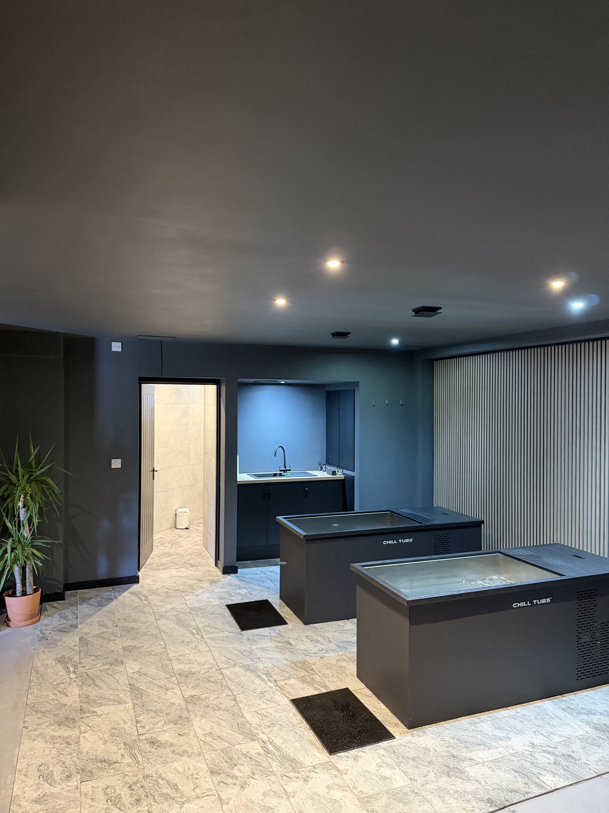 The ice bath room at RE:UP Altrincham: two Chill Tubs cold plunge baths on a stone floor, with the shower room doorway and a sink behind
