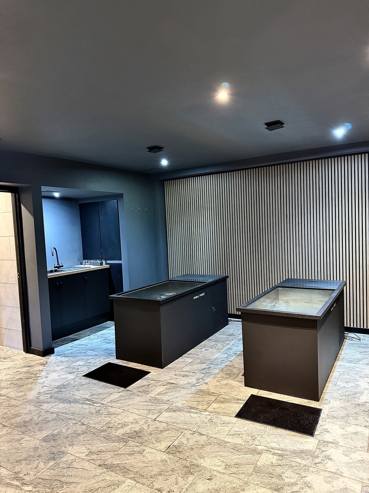 Two cold plunge ice baths side by side at RE:UP Altrincham, in front of a slatted timber wall